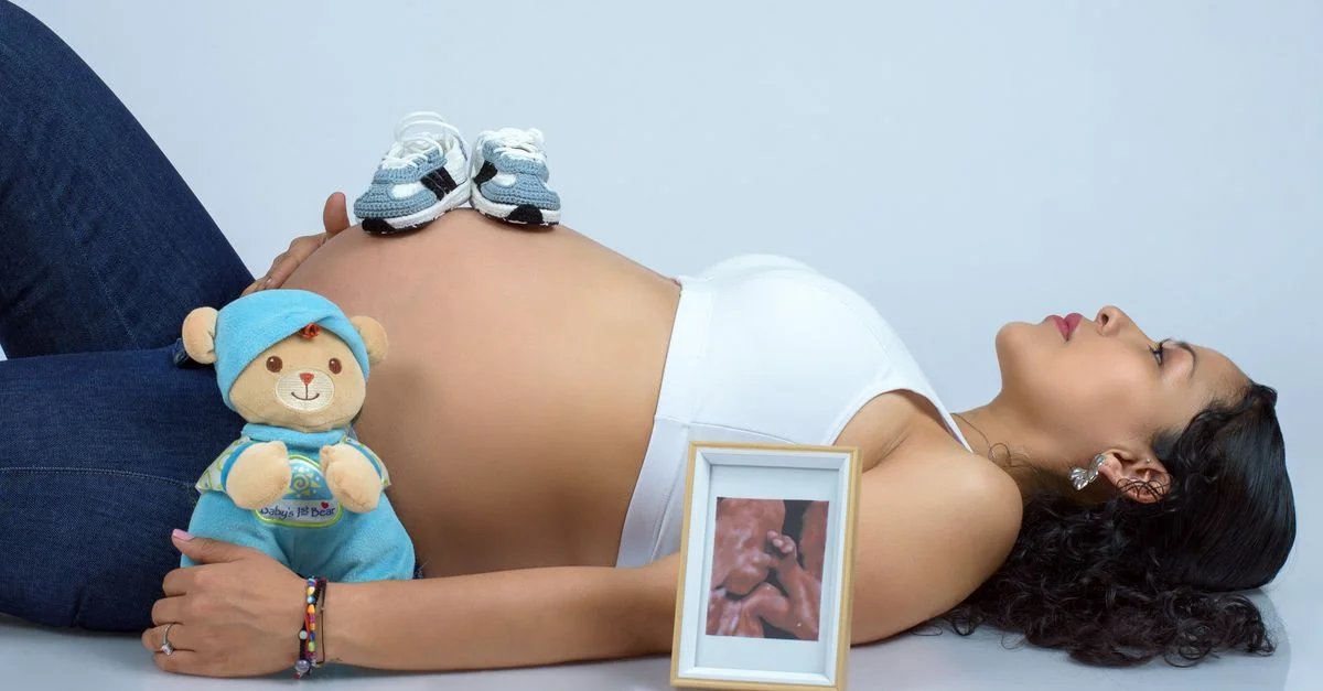 Mujer embarazada acostada con zapatos de bebé, foto de ecografía y peluche. Hermosa imagen de maternidad.