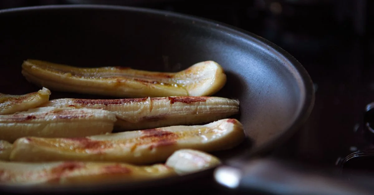 Plátanos en rodajas siendo fritos en una sartén antiadherente, capturando un delicioso momento culinario.
