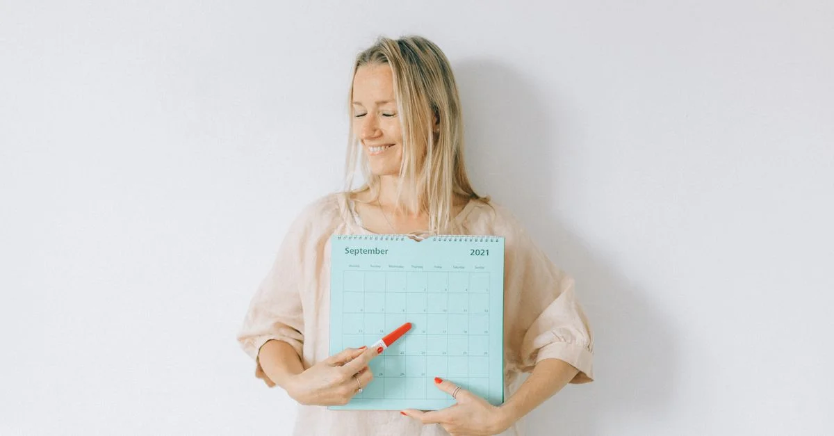 Mujer sonriente señala una fecha en un calendario, transmitiendo emoción y anticipación.