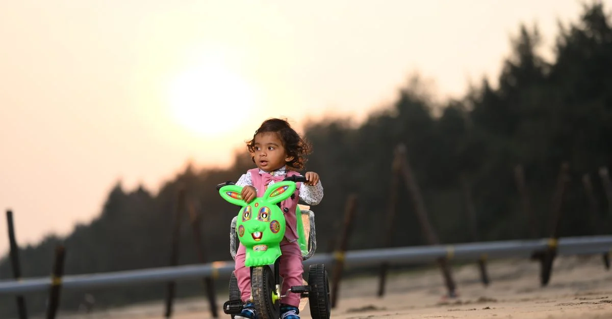 Un enfant profite d'une balade en tricycle sur une plage de sable au coucher du soleil à Tuni, en Inde.
