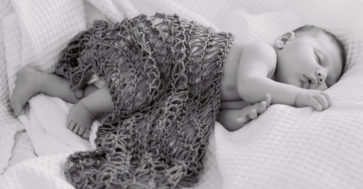 Adorable imagen en blanco y negro de un bebé durmiendo pacíficamente bajo una manta de punto.