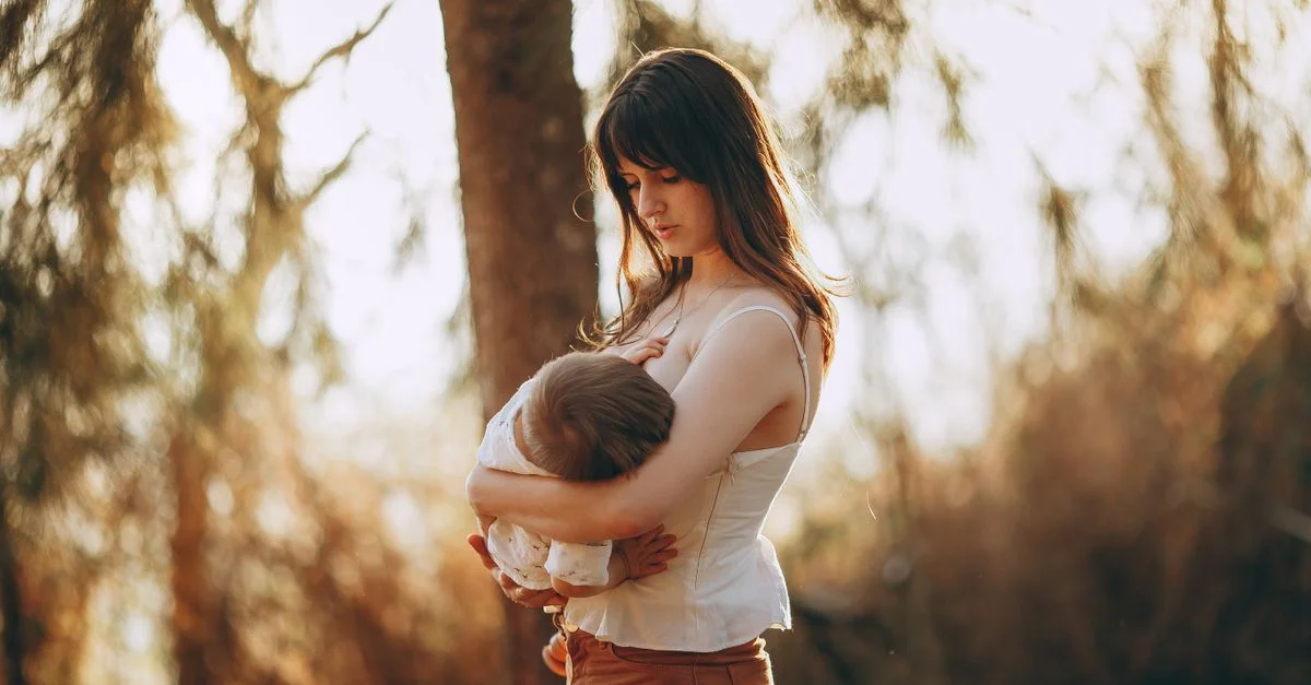 Una escena serena de una madre sosteniendo suavemente a su hijo en un parque soleado, capturando amor y calidez.