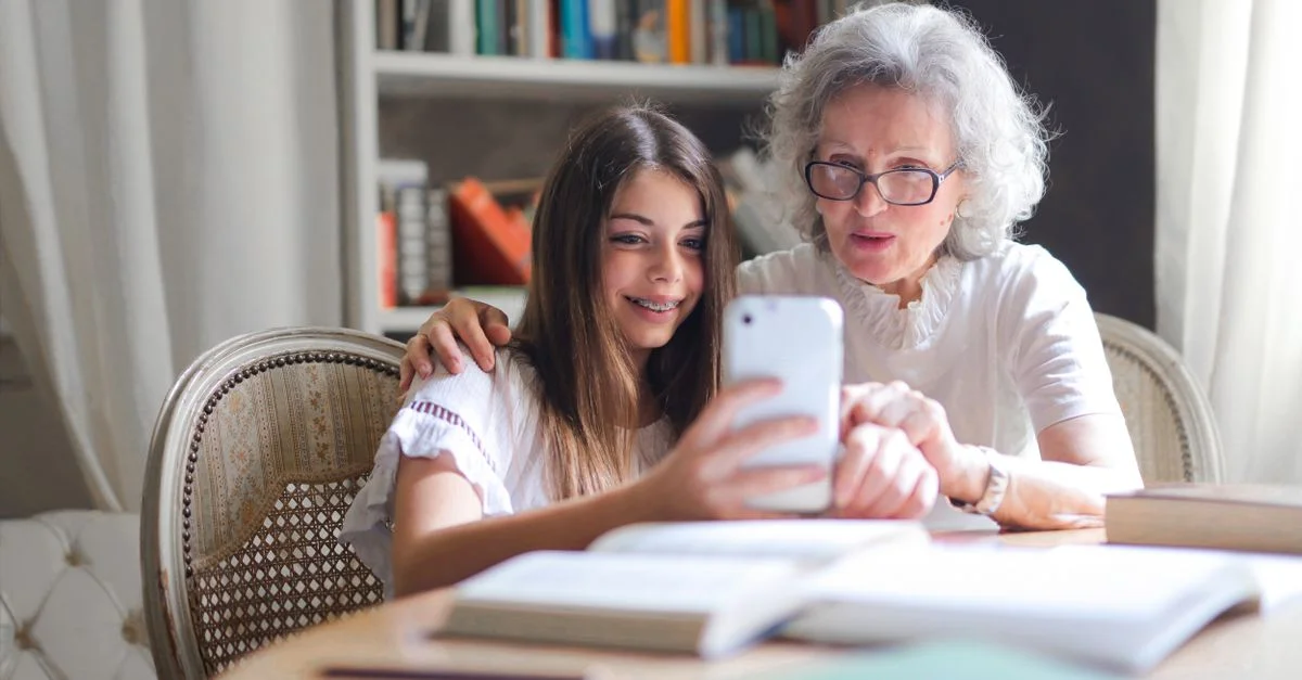 Una abuela y una nieta fortaleciendo su vínculo a través de un smartphone en casa, mostrando la conexión generacional.