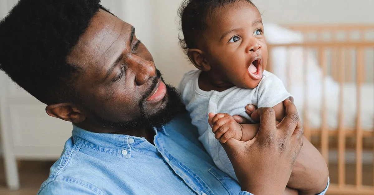 Moment tendre d'un père tenant son bébé souriant dans un environnement de nursery confortable.