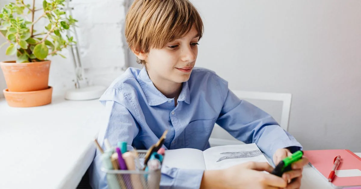 Un niño con una camisa azul usando una calculadora en su escritorio, enfocado en aprender y en la educación.