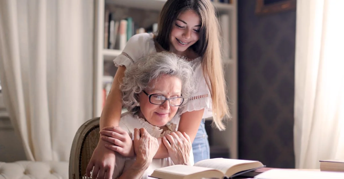 Un momento conmovedor de una nieta abrazando a su abuela mientras leen un libro juntas en el interior.