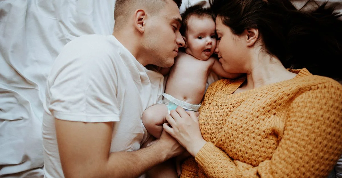 Un tierno momento familiar con los padres abrazando a su bebé en una cama acogedora, simbolizando amor y vínculo.