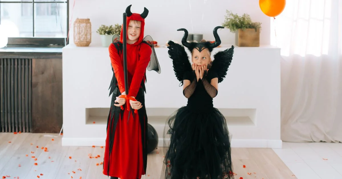 Dos niños disfrazados de diablo celebran Halloween en interiores, rodeados de globos festivos.