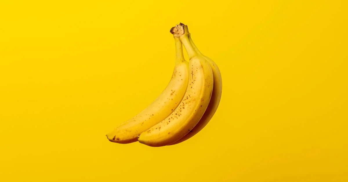 Un racimo de plátanos amarillos maduros contra un fondo amarillo vibrante, ofreciendo frescura tropical.