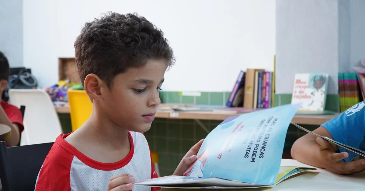 Un jeune garçon absorbé par la lecture d’un livre dans une salle de classe, favorisant l’alphabétisation des enfants.