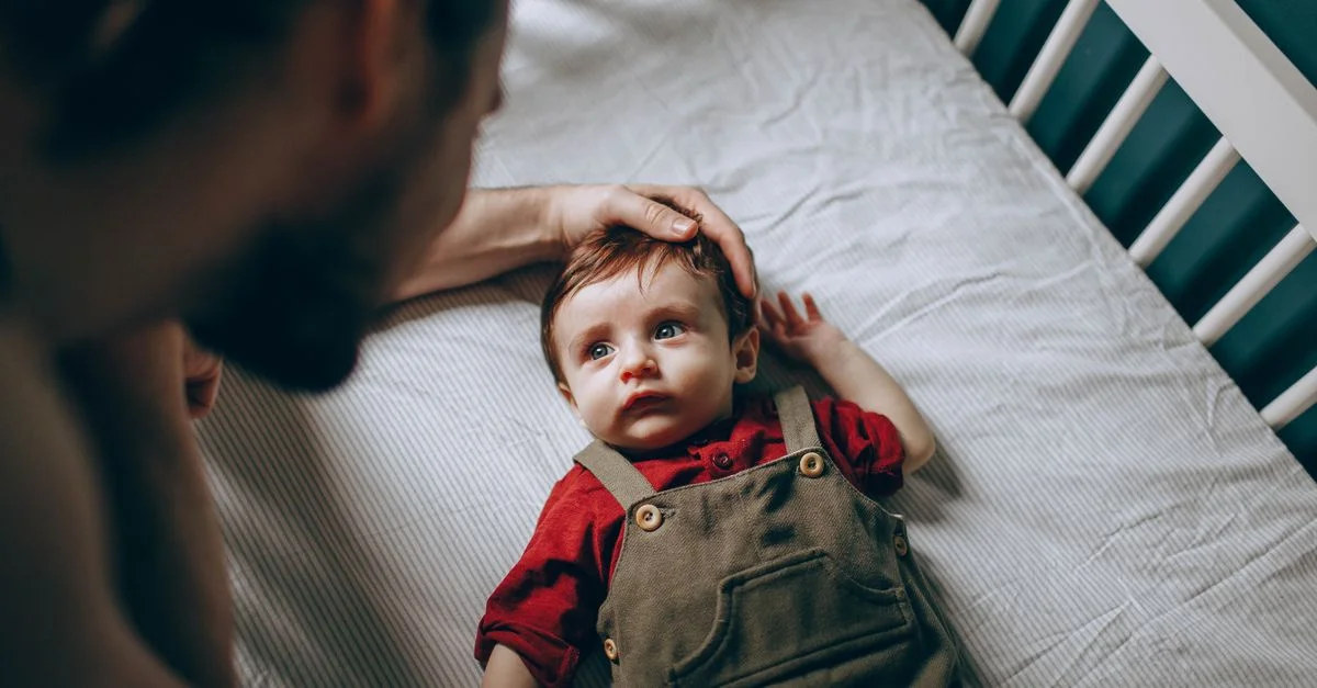 Un père caresse avec amour son bébé dans un berceau, montrant un moment tendre de la parentalité.