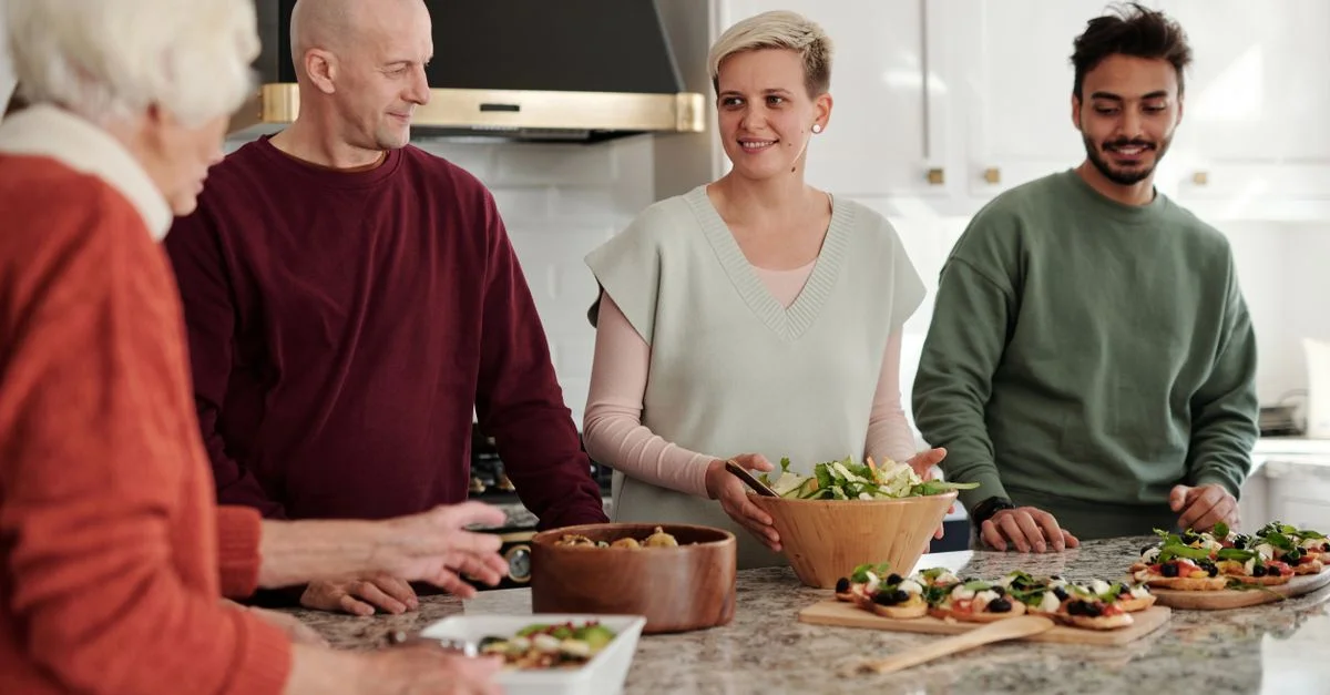 Miembros de la familia preparando y disfrutando de una comida juntos en un acogedor ambiente de cocina.