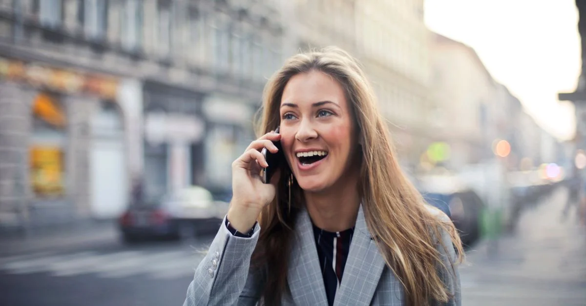 Femme joyeuse discutant au téléphone mobile tout en marchant dans une rue urbaine animée à Budapest.